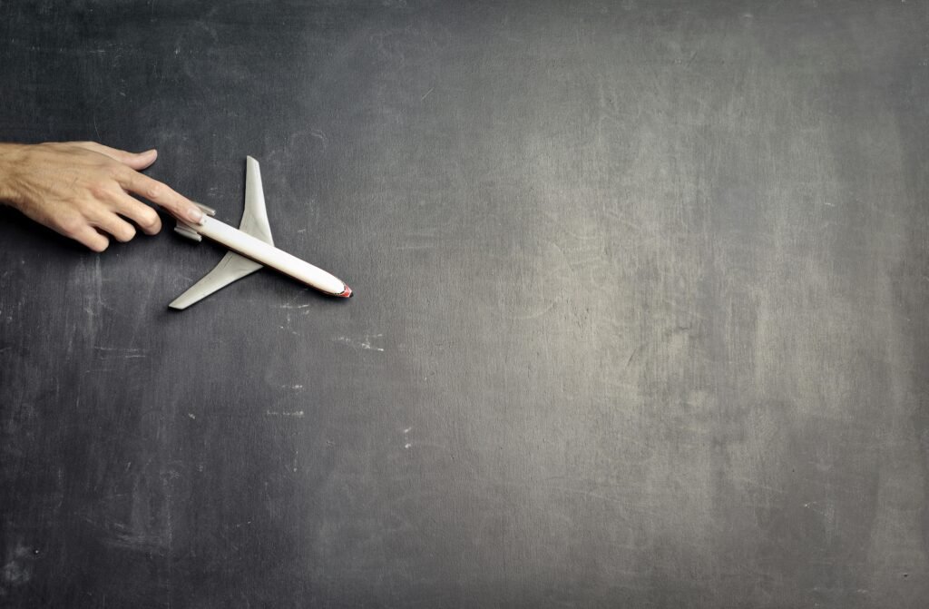 Top view of crop anonymous person driving toy airplane on empty blackboard while representing journey concept